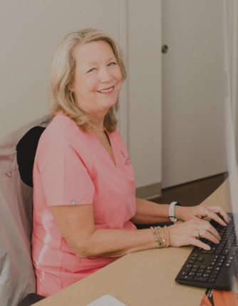 Smiling dental team member at computer behind reception desk