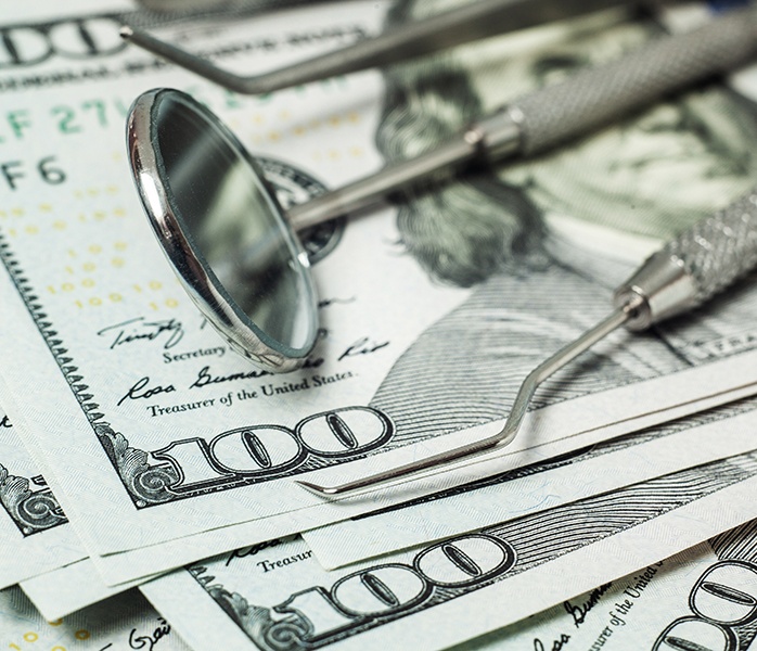 Dental tools lying on a large stack of hundred-dollar bills