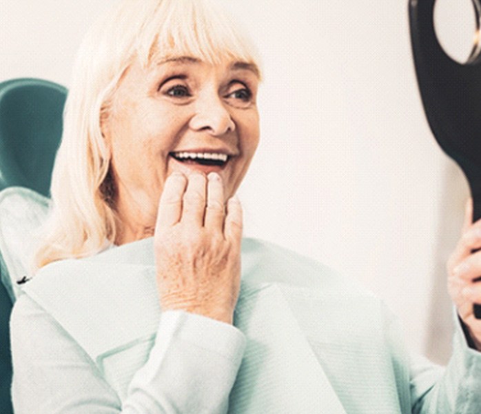 An older woman looking at her dentures in a hand mirror