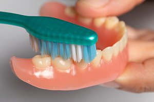 A patient cleaning their denture with a toothbrush