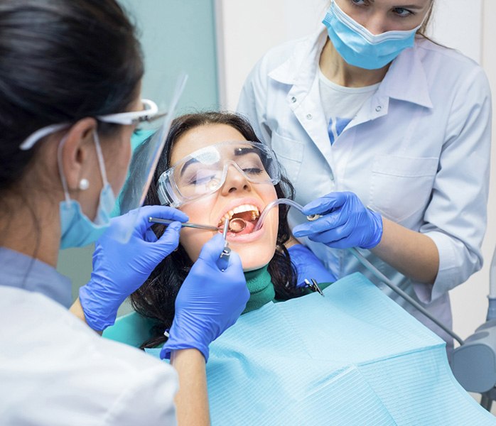 Two dentists in blue gloves performing procedure on patient whose eyes are closed