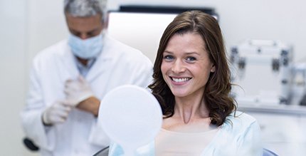 Woman with dental implants in Millersville smiling and holding mirror