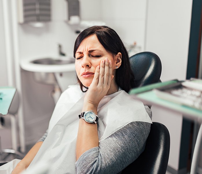 A woman rubbing her aching cheek at a dental appointment