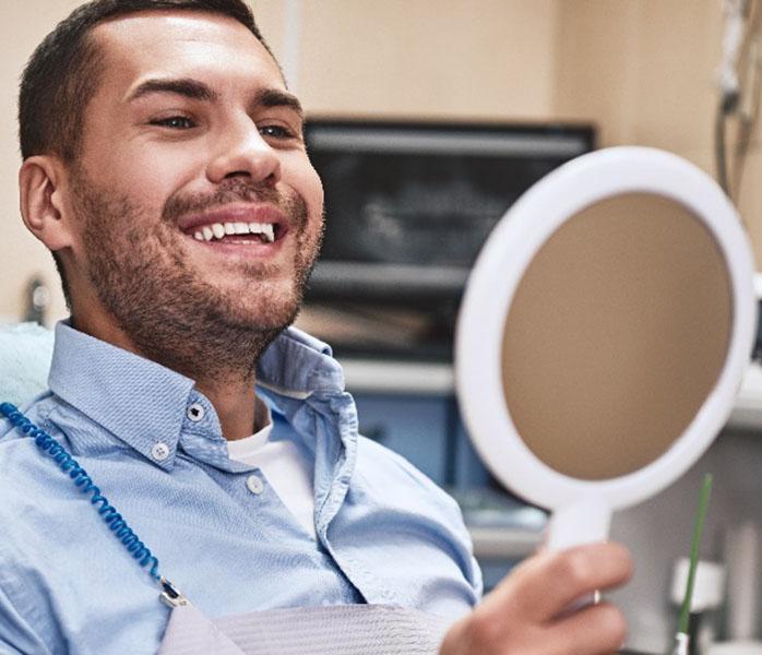 Man smiling while holding handheld mirror