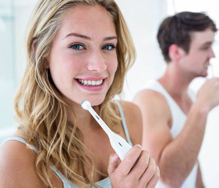 Woman smiling while brushing her teeth in bathroom with partner