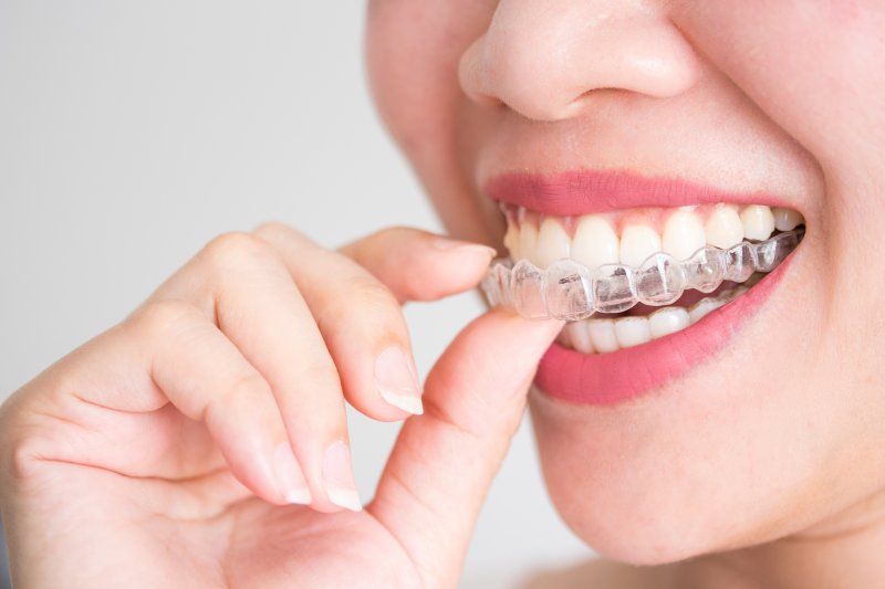 smiling woman putting Invisalign aligners in mouth